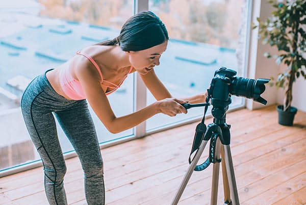 Blogger near window. Slim dark-haired fitness blogger standing near window using camera