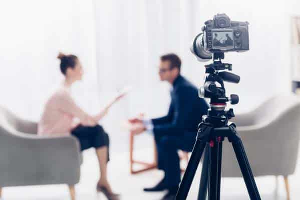 businessman giving interview to journalist in office, camera on tripod on foreground