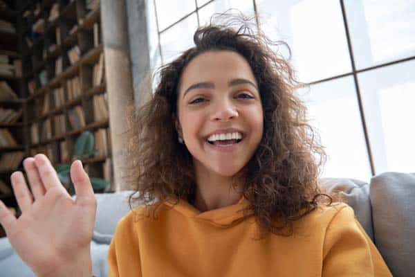 Happy hispanic latin gen z teen girl blogger smiling face waving hand talking to webcam recording vlog, social media influencer streaming, making video call at home. Headshot portrait. Webcamera view