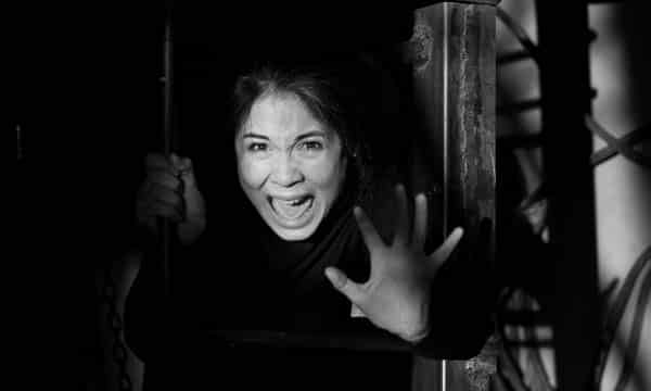 A black and white portrait of the emotional and screaming from fear of a woman with dark hair, looking frightenedly not light putting her hand in front of her in the dark room of an abandoned building