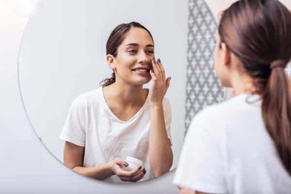 Face cream. Young beautiful woman wearing white shirt putting face cream on her nice healthy skin